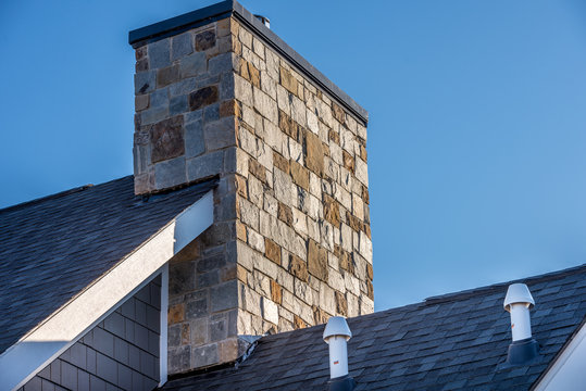 Large Stone Cladding covered masonry chimney on top of a asphalt roof at a new USA residential construction project