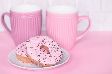 pink coffee cups and doughnuts with pink frosting in a plate close-up. pink background with drinks in cups and donuts on a plate.