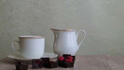 white porcelain cup with creamer and dark chocolate candies decorated with dried berries on a...