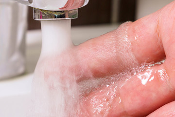 checking the temperature by touching the running water with your hand. Close-up on fingers under hot water from the tap sink or bath in the bathroom at home