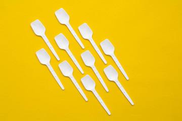 White plastic spoons on yellow background. Fast food, eco and no plastic concept. Top view. Copy, empty space for text