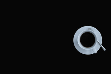 Top view of a white coffee cup with saucers and spoons  on the right side of the black background, there is a space  for  text.