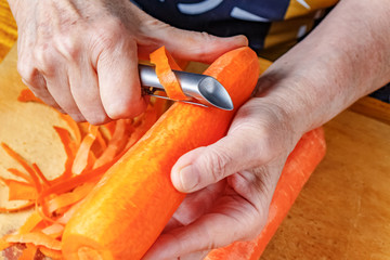 Peeling fresh bright orange carrot by peeler for vegetables and fruits