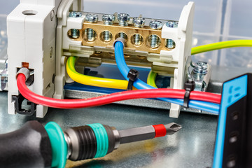 Installed wire terminal on metal mounting plate of electrical panel with connected colored wires and screwdriver on foreground. Electrical panel assembling