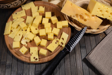 Close-up. On a cheese board lies sliced cheese. Nearby is a plate of uncut cheese and a knife.
