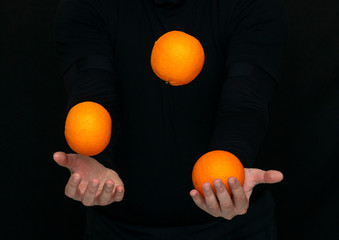 male hands juggle with fresh oranges on a dark background