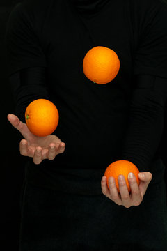 male hands juggle with fresh oranges on a dark background