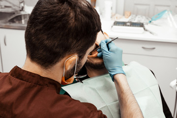 A young male dentist doctor treats a patient. Medical manipulations in dentistry, surgery. Professional uniform and equipment of a dentist. Healthcare Equipping a doctor’s workplace. Dentistry