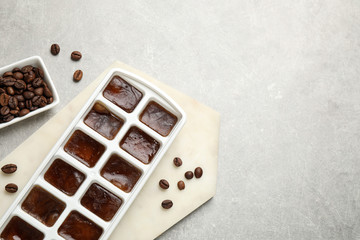Ice cubes with coffee beans in tray on grey table, flat lay. Space for text