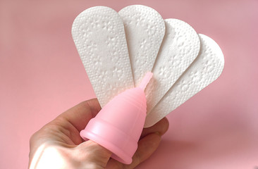 Obraz premium Menstrual cup and daily sanitary pads in a female hand on a pink background, hygiene and cleanliness, woman's health