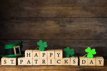 Wooden cubes with words HAPPY ST PATRICK'S DAY, green leprechaun hat and clover leaves on table