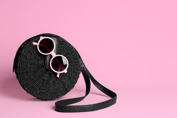 Stylish woman's bag and sunglasses on light pink background. Space for text
