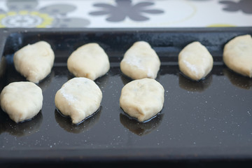 Pies on a baking sheet ready for baking. The bun shaped dough lies on a black baking sheet. Home baking cooking process.