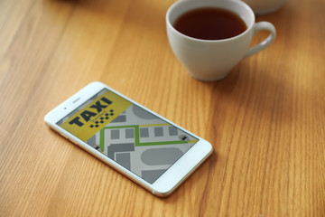 Smartphone with taxi application and cup of tea on wooden table