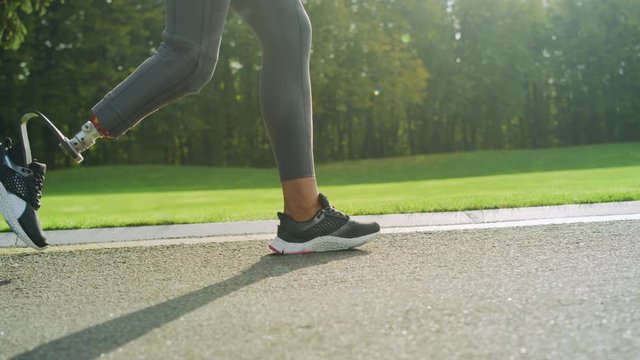 Disabled woman in sports shoes running on road. Girl feet training outdoors