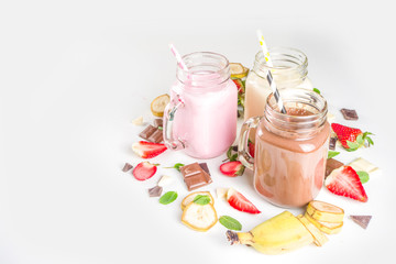 Three mason jars with milkshakes or smoothie. Summer healthy breakfast, lunch drinks - banana, chocolate and strawberry milkshakes on wooden background