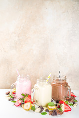 Obraz na płótnie Canvas Three mason jars with milkshakes or smoothie. Summer healthy breakfast, lunch drinks - banana, chocolate and strawberry milkshakes on wooden background