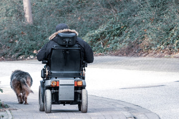 old man drives an electric wheelchair and is accompanied by his faithful dog