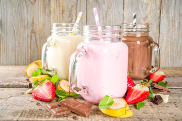 Three mason jars with milkshakes or smoothie. Summer healthy breakfast, lunch drinks - banana, chocolate and strawberry milkshakes on wooden background