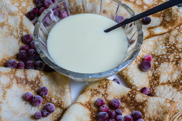 Maslenitsa: thin pancakes with berries and a glass of milk on a wooden table.