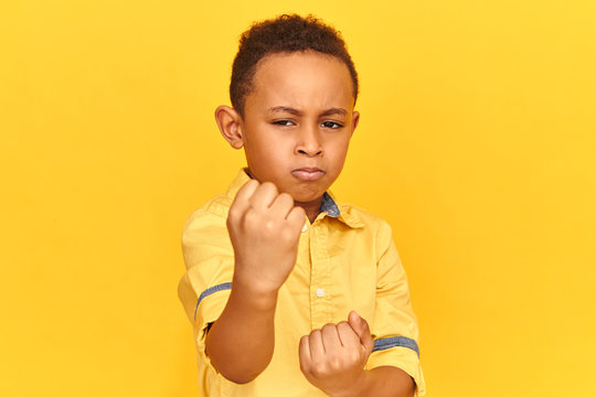 Studio image of angry serious Afro American little boy frowning eyebrows, showing clenched fist at camera, making warning gesture, affronting bully, can stand up for himself. Selective focus