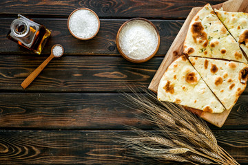 Focaccia ingredients. Wheat ears, flour, oil near bread on dark wooden background top-down copy space