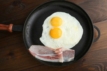two fried eggs is on the pan on dark wooden background