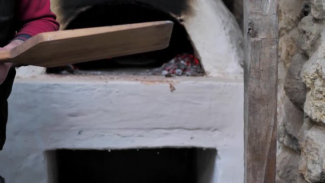 The man put the raw flatbread on a wooden spatula and put it in the oven.