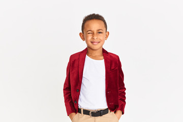 Portrait of adorable fashionable African American boy with curly short hair holding hands in pockets and winking at camera having confident look. Style, beauty and children&rsquo;s fashion concept
