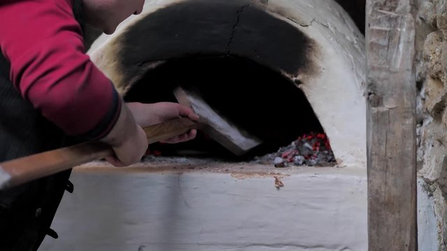 The man put the raw flatbread on a wooden spatula and put it in the oven.