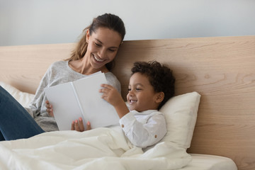 Smiling mother with African American child reading book in bed
