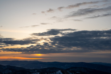 sun hiding behind clouds at sunrise in winter mountains, slovakia low tatras, dumbier