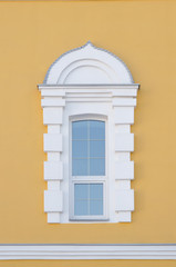 Vintage elongated white window with arched arch on a yellow wall. Beautiful architecture. Framing of white squares, at the bottom of the picture is a cornice. Decorative stripes on glass, metal tides © Sergei