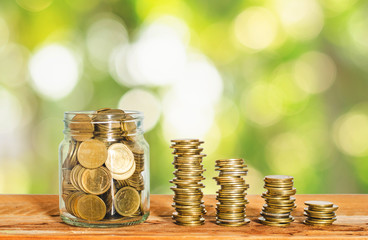 golden coin in glass jar with money stack on wood table with green blur nature background. business financial banking saving concept. investment profit income. startup. successful.