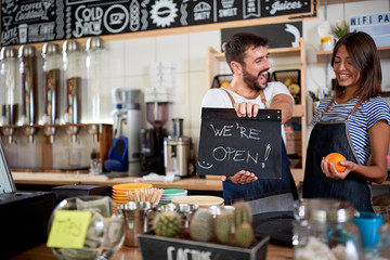 Man and woman  in their cafe store showing open sign.