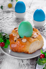 Easter yeast bun ring with almond and colored egg in the middle on the white wooden table