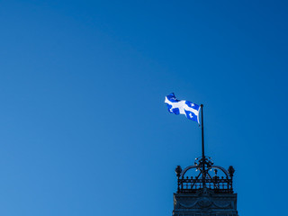 Floating blue flag with lys flowers from Quebec over the parliament building with blue sky