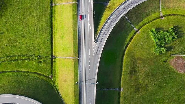 Aerial shot of a  highway road with interception passing through the rural countryside and green forest with moving cars and transport, top down view