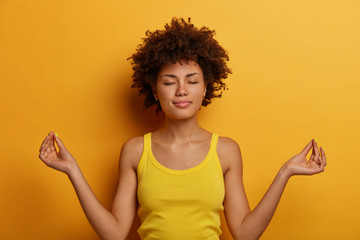 Peaceful calm curly woman stands in lotus pose, reaches nirvana, practices yoga or meditation,...