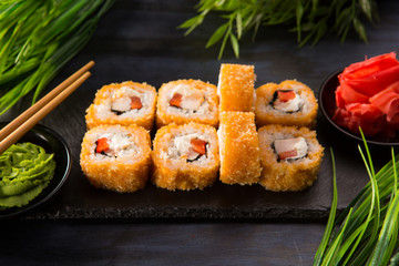 Set of baked sushi rolls with wasabi and ginger on a black background. Japanese oriental cuisine