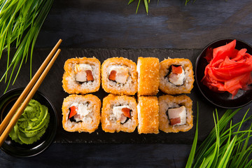 Set of baked sushi rolls with wasabi and ginger on a black background. Japanese oriental cuisine