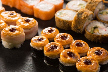 Set of baked sushi rolls with wasabi and ginger on a black background. Japanese oriental cuisine