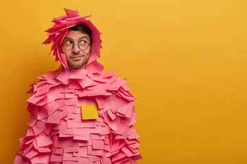 Indoor shot of male advertiser or manager covered with sticky adhesive notes, looks aside as...