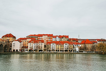 Obraz premium Houses with red roofs along the Drava River. Autumn or winter in a European city. Maribor city, Slovenia, Europe.