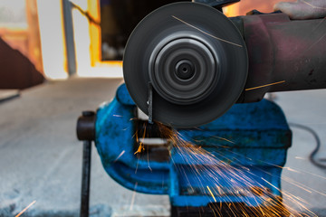 Man with an angle grinder cutting a piece of metal on a vise