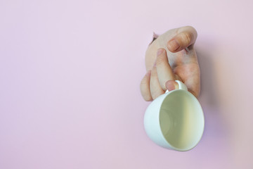 Trend-hand through a hole in a pink background with an empty white coffee Cup with space to copy