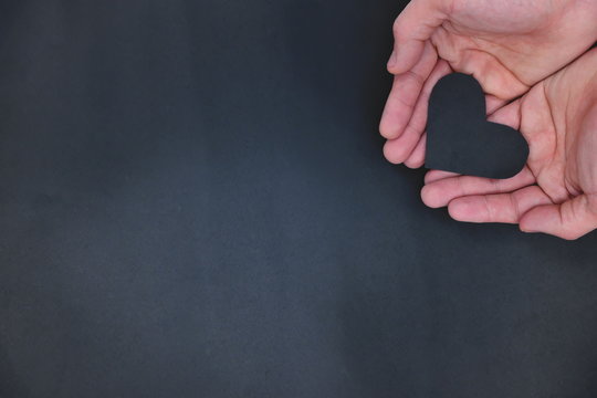 Hands holding a black heart in black background. Black lives matter, unhealthy heart and  life insurance concept. Top view with copy space.