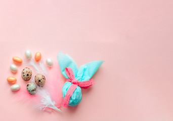 Egg gift in green paper packaging and with pink ribbon Easter Bunny wrap idea. Chocolate dragee white and gold color, multicolor colorful feathers. Minimal concept. Flat lay, Copy space, top view