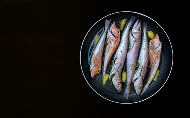 The concept of simple healthy food. Fresh sea fish in oil prepared for frying in a pan with herbs and lemon on a black background. Mediterranean diet. Food photo, horizontal orientation,  copy space