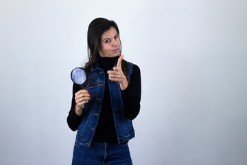 Fototapeta premium Portrait of confident ambitious successful attractive caucasian middle age woman model with magnifying glass looking directly at camera, showing direction with one forefinger, isolated on gray backgro